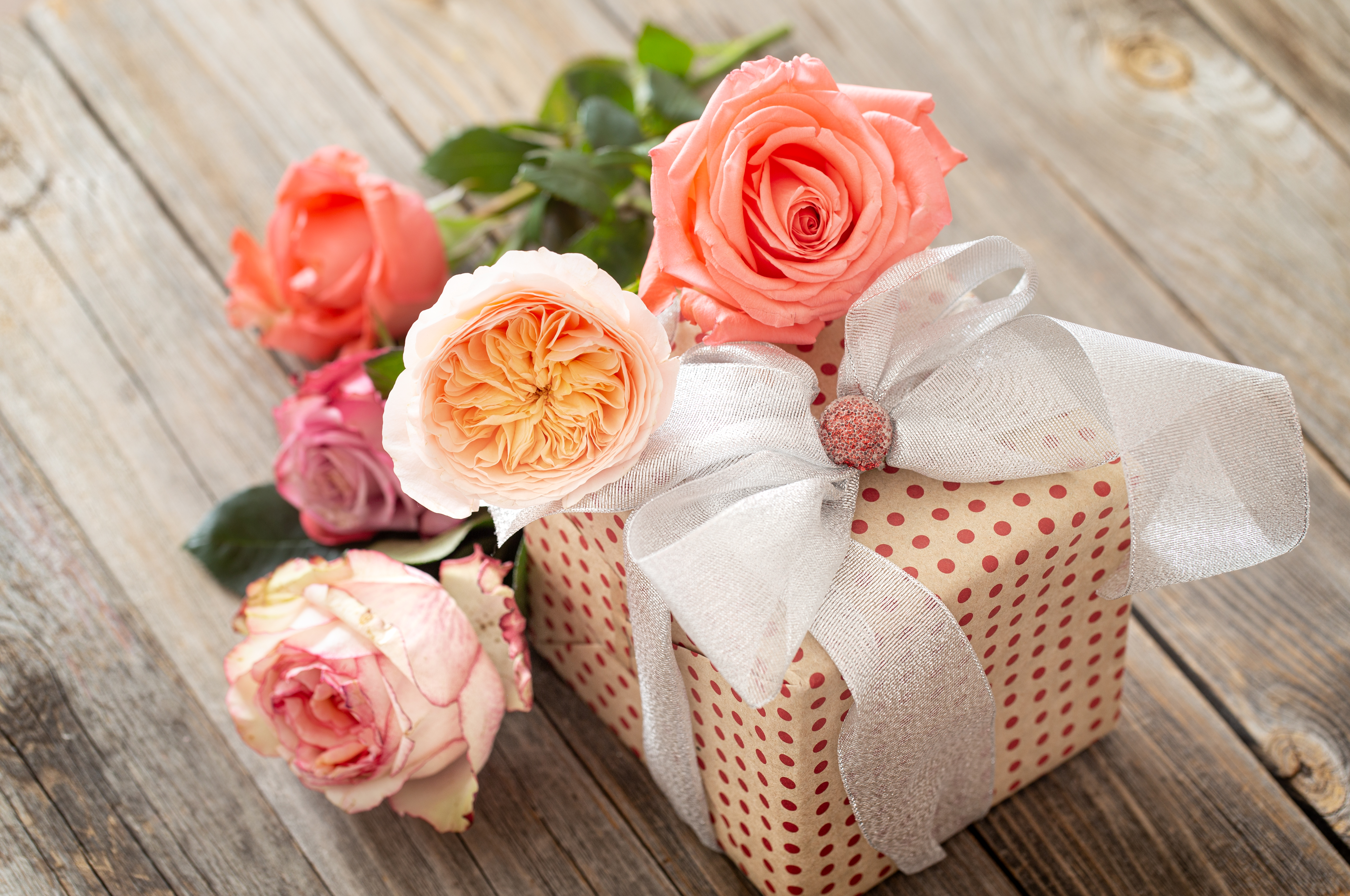 beautifully-wrapped-gift-and-a-bouquet-of-roses-on-a-blurred-wooden-table